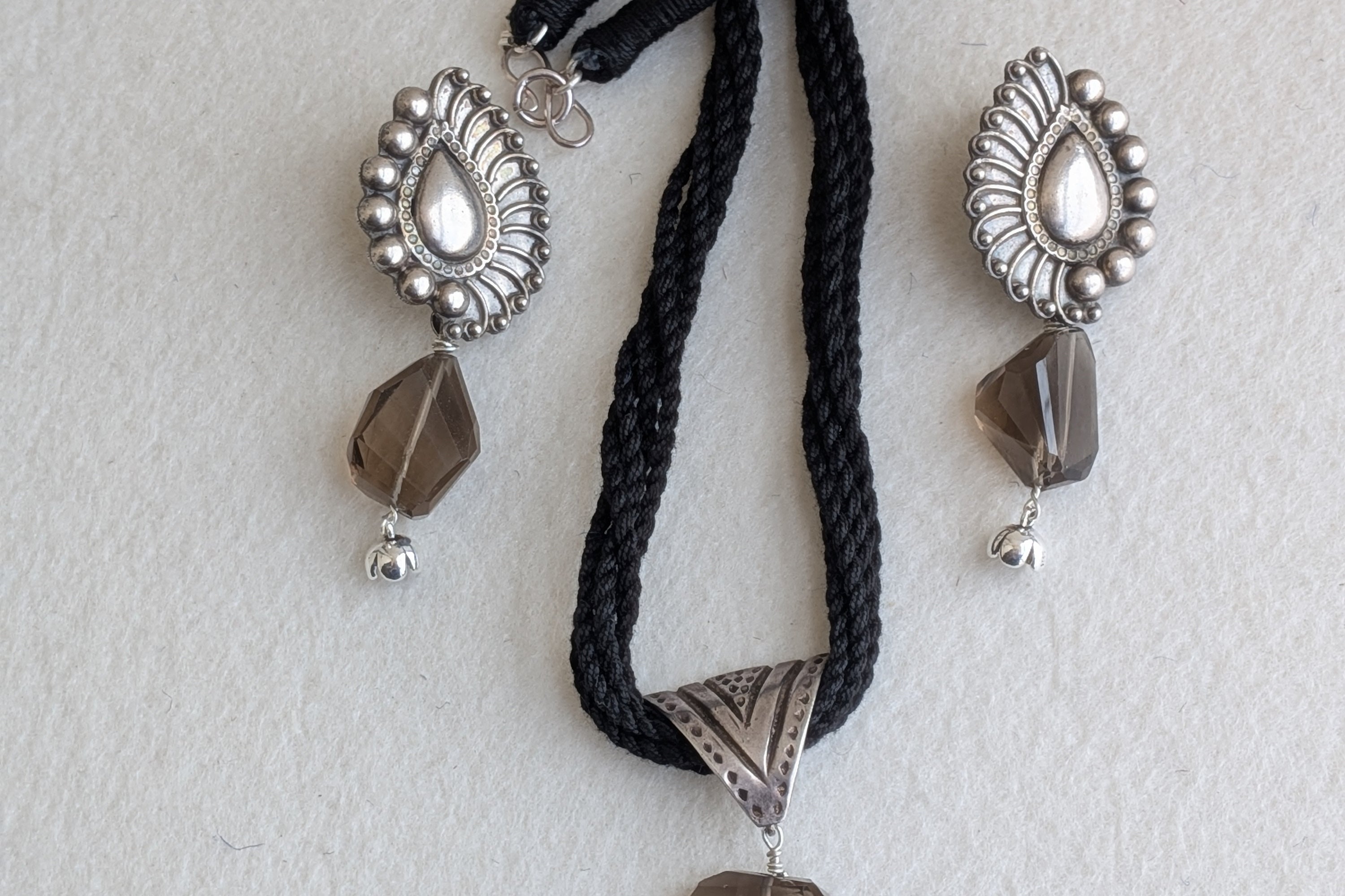 Handcrafted 925 silver jewelry set with triangle pendant and peacock feather earrings, adorned with smokey quartz. Perfect for weddings and festivals