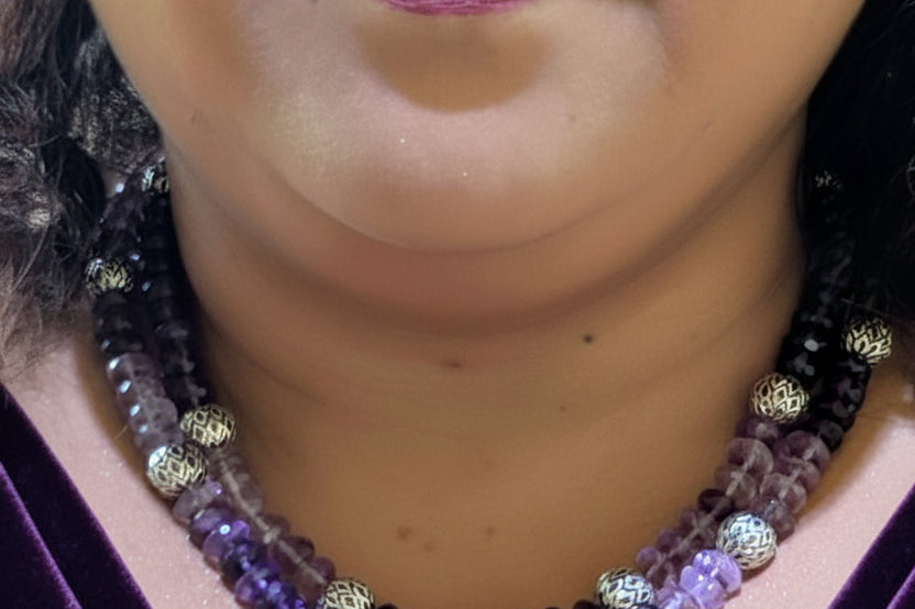 Close-up of a person wearing a beaded necklace with purple and gold beads.