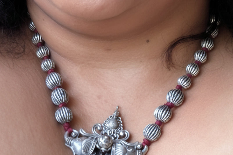 Close-up of a person wearing a silver necklace with a decorative pendant.