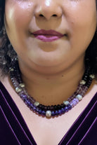 Close-up of a person wearing a beaded necklace with purple and gold beads.