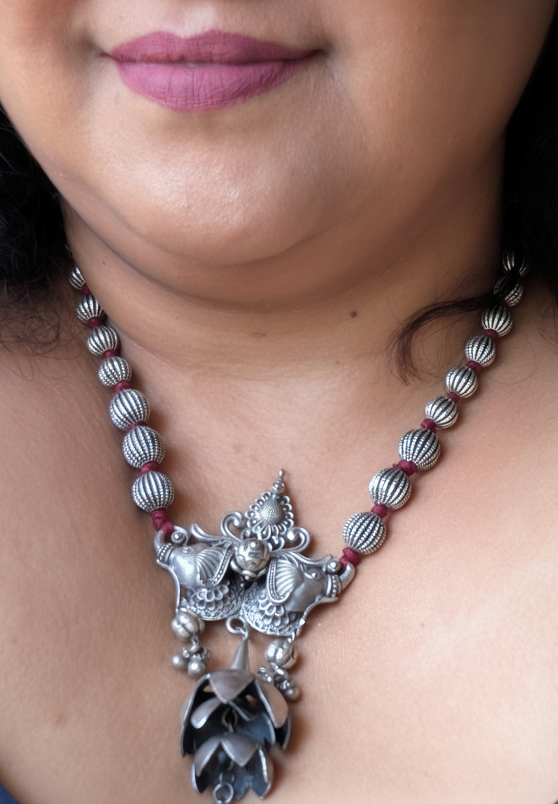 Close-up of a person wearing a silver necklace with a decorative pendant.