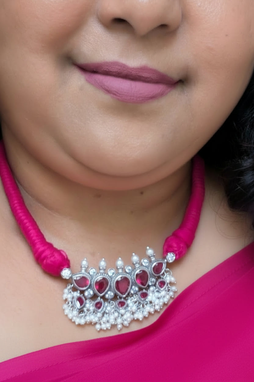 Close-up of a person wearing a silver necklace with red stones and pink thread.